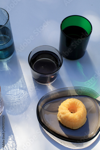 Glasses of water and lemon pound cake bath bokeh sunlight colorful reflect on white background. Modern minimal elegant aesthetic.