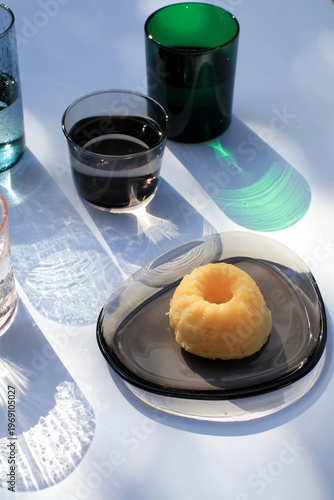 Glasses of water and lemon pound cake bath bokeh sunlight colorful reflect on white background. Modern minimal elegant aesthetic.