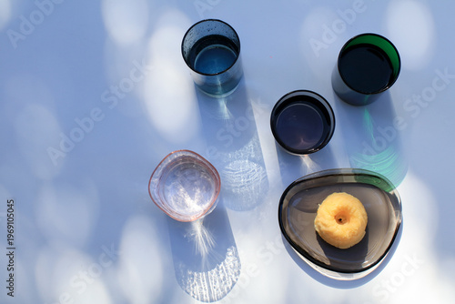 Glasses of water and lemon pound cake bath bokeh sunlight colorful reflect on white background. Modern minimal elegant aesthetic.