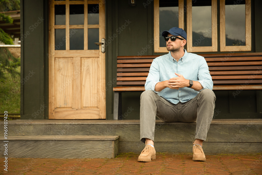 Fototapeta premium A man sits casually on steps outside a house, space for text