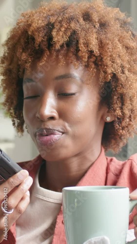 Vertical video: Lifting phone woman in rust jacket reading lines aloud in kitchen holding green mug