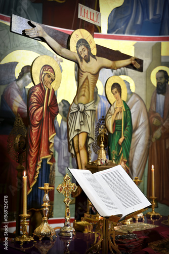 Orthodox Christian Altar with Open Liturgy of St. Basil Book end Candlelight. Crucifixion of Jesus with grieving figures of Mary and John all out of focus in Warm Sacred Interior.