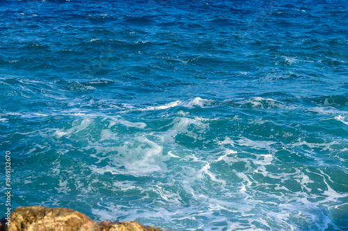 Gentle waves lap against the rocky shore under the bright sun on a serene summer day.