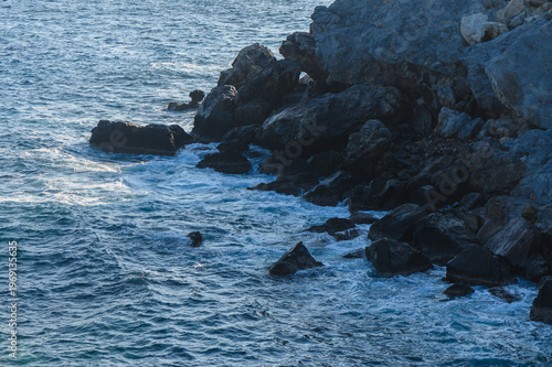 Waves crashing against rugged coastal rocks at twilight along the serene seashore.