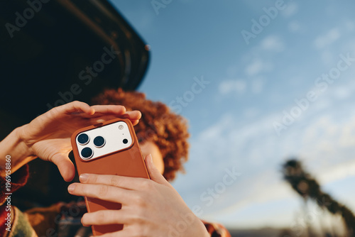 Photos Woman with curly hair wearing rainbow sweater taking photo with smartphone outdo