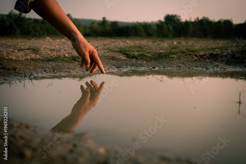 Hand touching water reflection in dry landscape during drought.
