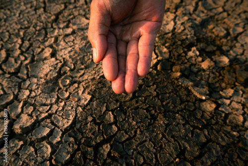 Hand catching scarce water drops over severely cracked drought soil under extreme dryness.