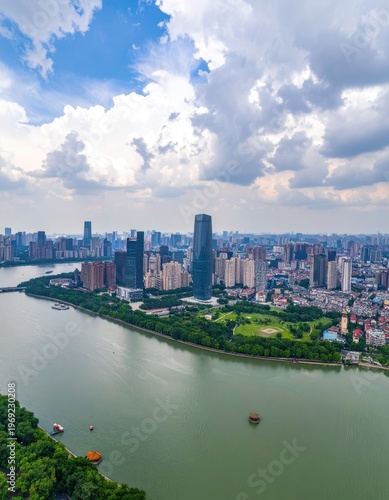 An aerial view showcases a sprawling cityscape nestled along a winding river, framed by a dramatic sky filled with fluffy white clouds.