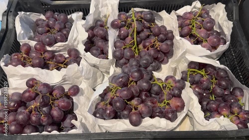 Bunches of grapes arranged in trays at a market stall during the afternoon hours in a busy town