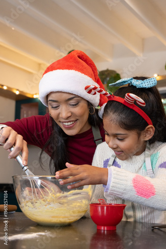 Asian mother and daughter mixing batter in kitchen with clear glass bowl whisk, candy-cane hats