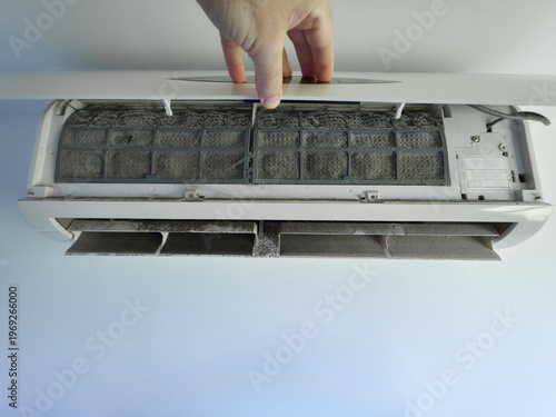 Hand opening a dirty air conditioner revealing dust-covered filters