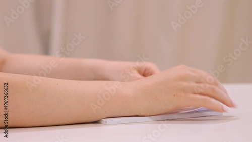 Woman is sitting at a table with her hands on it. She is holding a white object in her right hand