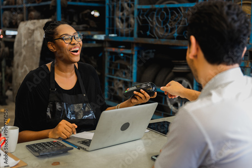 Female mechanic processing card payment with customer at auto repair shop counter