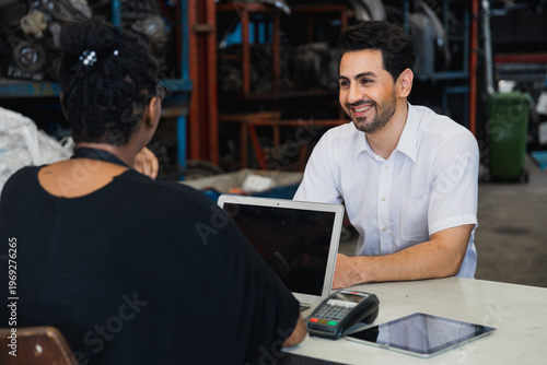 Customer consulting with mechanic at auto repair shop counter using laptop