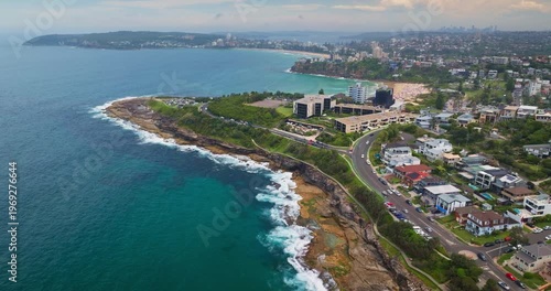 Sandstone coastline of Sydney's North Head, with turquoise ocean waves crashing against cliffs and the distant Manly beach, suburbs city skyline. Modern coastline cityscape aerial drone view flight