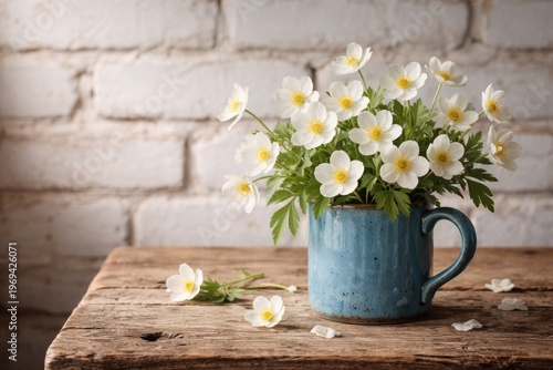 Rustic spring scene with white anemone flowers arranged in a blue ceramic mug on wooden table and white brick wall background with copy space