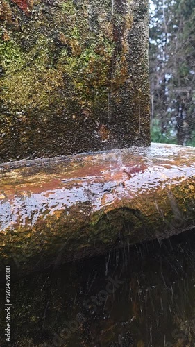 Rainwater is dramatically splashing and dripping onto a textured, moss-covered stone surface, highlighting the weathered details and natural erosion in an outdoor setting
