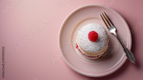 A single delicious raspberry sponge cake topped with powdered sugar served on a soft pink ceramic plate with a silver dessert fork in a minimalist studio setting
