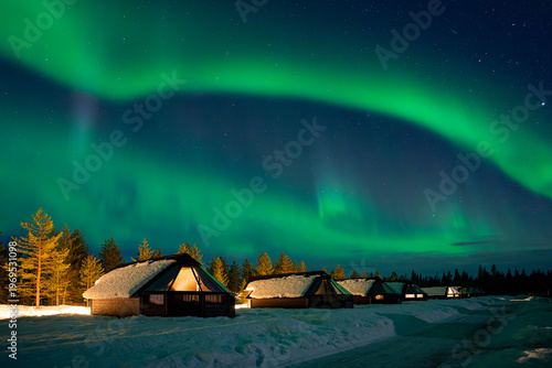 Snow-covered village, Lapland, Northern Finland, rural houses with glass roof, snow covered. Aurora borealis (also known like northern or polar lights) beyond the Arctic Circle. Levi, Finland