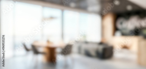 A modern office interior featuring a stylish meeting area with a round wooden table and comfortable chairs, illuminated by natural light from large windows.