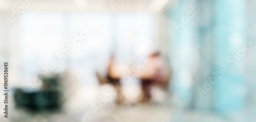 A blurred view of a modern office space with two individuals engaged in a discussion around a table, emphasizing collaboration and communication in a corporate environment.