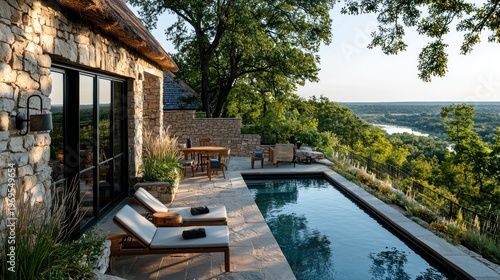 Luxury stone dwelling with a pool overlooking a lush valley and river. Features include patio furniture, vegetation, and a thatched roof
