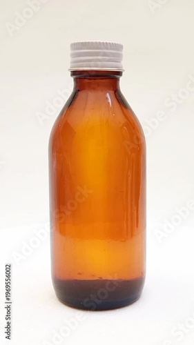 Amber glass bottle with cap rotating on white background, brown glass bottle for pharmaceuticals, syrups, essential oils, and cosmetics, vertical clip