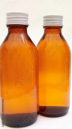Amber glass bottles with cap rotating on white background, brown glass bottles for pharmaceuticals, syrups, essential oils, and cosmetics, vertical clip