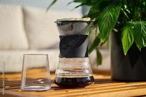 Konstfotografi Fresh brewed filter coffee in paper dripper above glass carafe on wooden table near houseplant