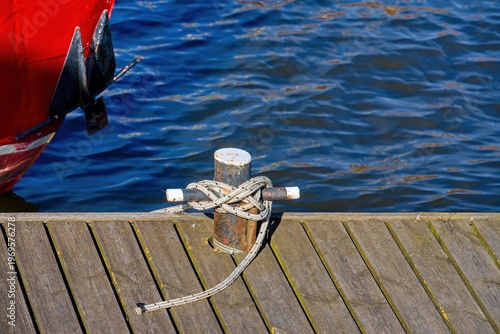 Fotografie Mooring rope tied to metal bollard on wooden pier