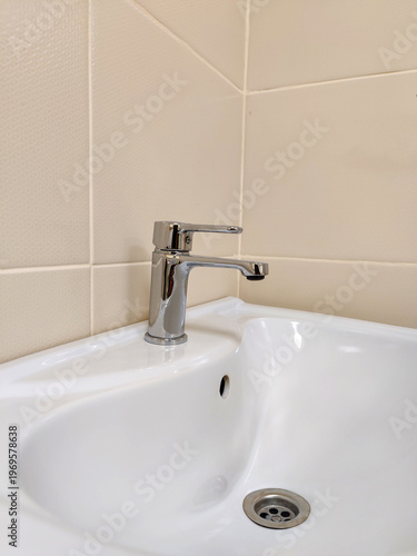 Modern single lever sink faucet mounted on white ceramic sink. Close-up. Copy space