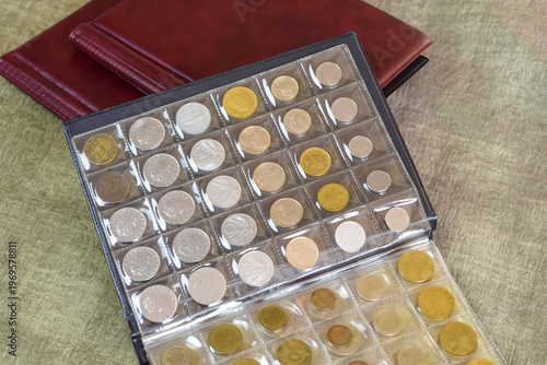 Pages from album full with old coins and burgundy albums for collecting coins. Coin storage method. Numismatic. Close-up. Copy space.