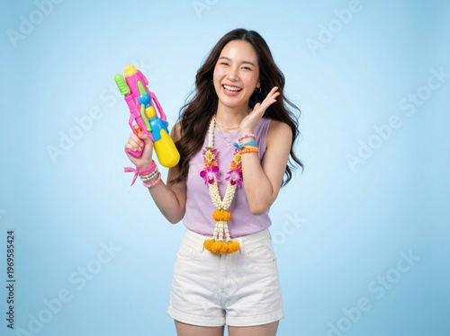 Asian woman holding colorful water gun wearing flower garland on blue background. Songkran water festival and tropical summer travel vacation thailand
