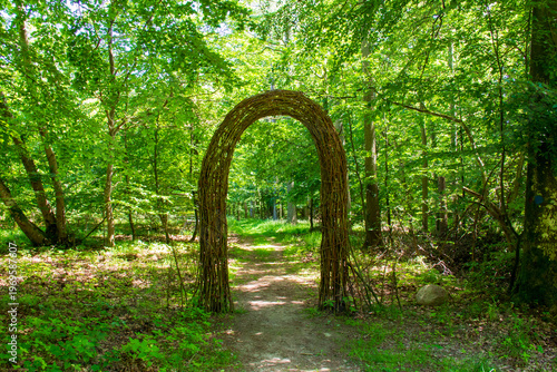 Woven wicker archway over a trail in a lush green forest