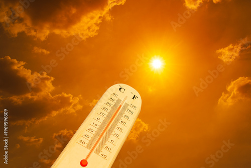 The thermometer against an orange sky. The thermometer is measuring the high summer temperatures, indicating scorching heat from global boiling. 