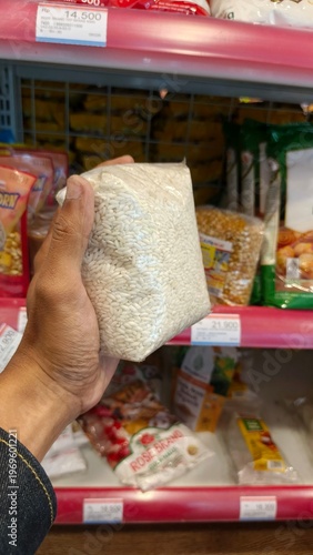 Sticky rice in small plastic bag held in hand at supermarket shelf. Grocery shopping and staple food concept.