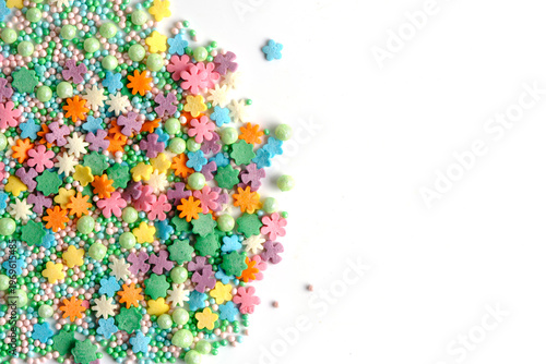 Colorful flower shaped sprinkles and pastel sugar pearls scattered on white background with copy space on right.