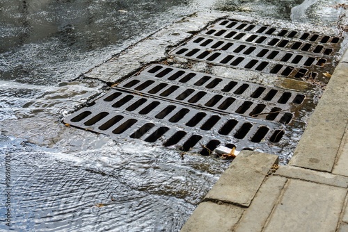 Stormwater rushing through metal grates along a curb, illustrating urban runoff and water management.