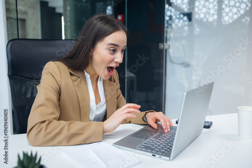 Surprised shocked businesswoman looking at laptop screen at office. Pretty girl suddenly excited with e-mail or news on Internet. Get promoted with salary increase.