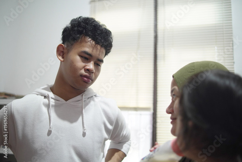 Happy young man talking to mother holding baby sister in candid family moment at home