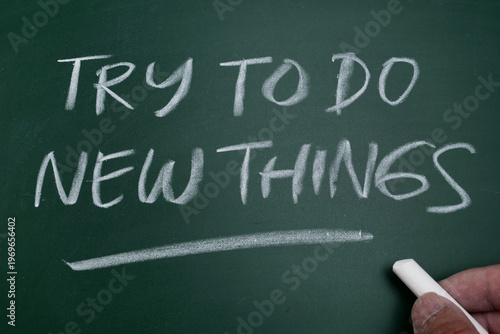 Hand writing inspirational quote 'Try To Do New Things' on a green chalkboard