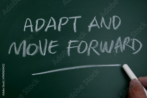 Hand writing motivational quote 'Adapt and Move Forward' on a green chalkboard