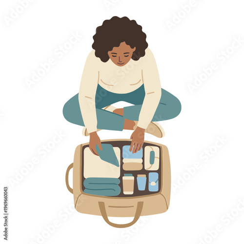 A woman sits cross-legged packing clothes and toiletries into an open suitcase