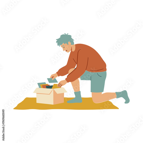 A man kneels on a mat unpacking items from a cardboard box.