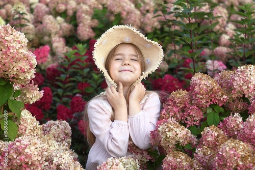 Adorable Little Girl Enjoying Nature Surrounded by Blooming Hydrangeas in a Summer Garden.