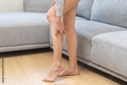 Muscle pain or leg pain, suffer asian young woman, girl hand massaging brawn leg calf muscle cramps or spasm, trauma from inflammation of tendon at calves while standing at home. Health care concept.