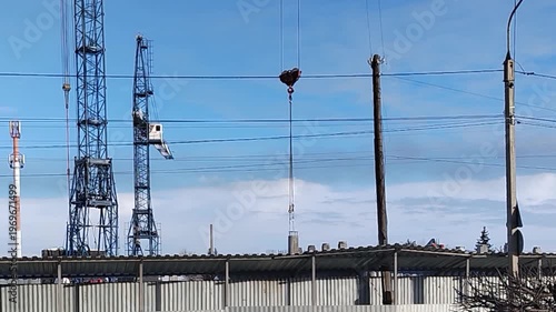 Crane lifting a load above a construction site with blue sky and power lines visible, showcasing the operation of heavy machinery in an industrial setting