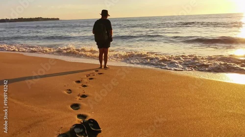 Lonely Traveler Walking Barefoot on a Golden Sandy Beach at Sunset, Leaving Footprints