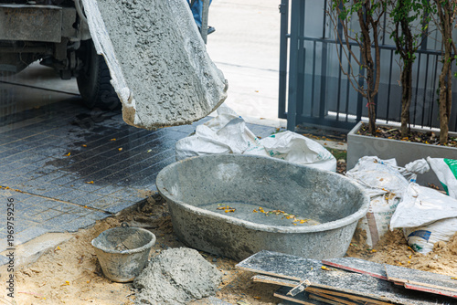 Pouring wet cement concrete from a truck mixer chute into a large mixing tub at a residential construction site. Professional building process and infrastructure development.