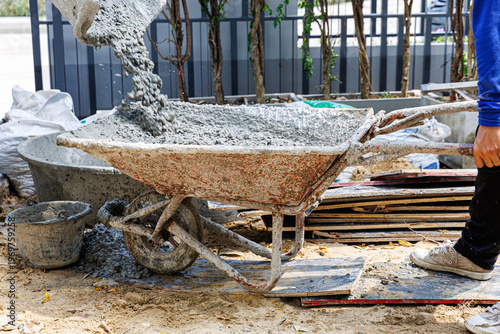 Pouring wet cement concrete from a truck mixer chute into a large mixing tub at a residential construction site. Professional building process and infrastructure development.